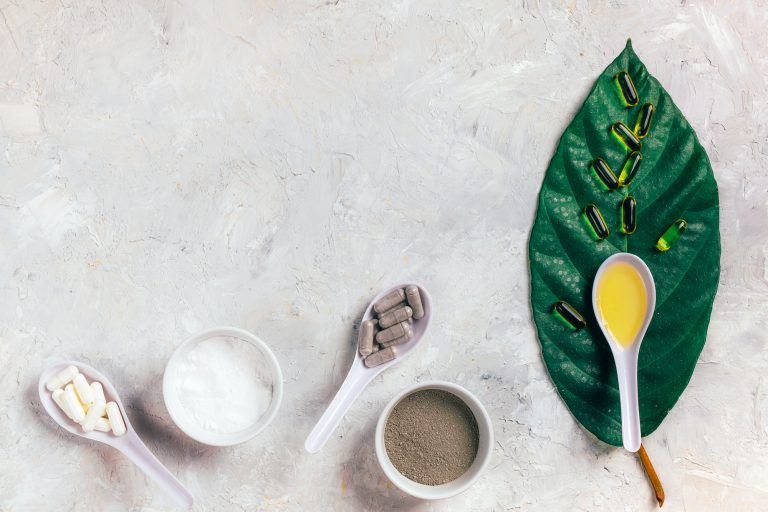 Capsules fish oil omega-3, white and gray pills, powder and oil in spoons on the green leaf